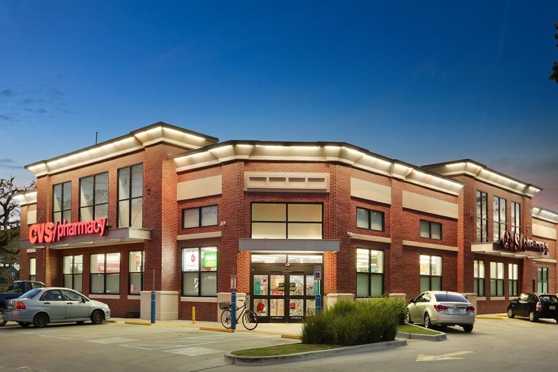 Exterior view of a CVS Pharmacy store at twilight, showcasing its bright signage and brick facade involved in past zero-cash-flow transactions, with parked cars and clear skies.