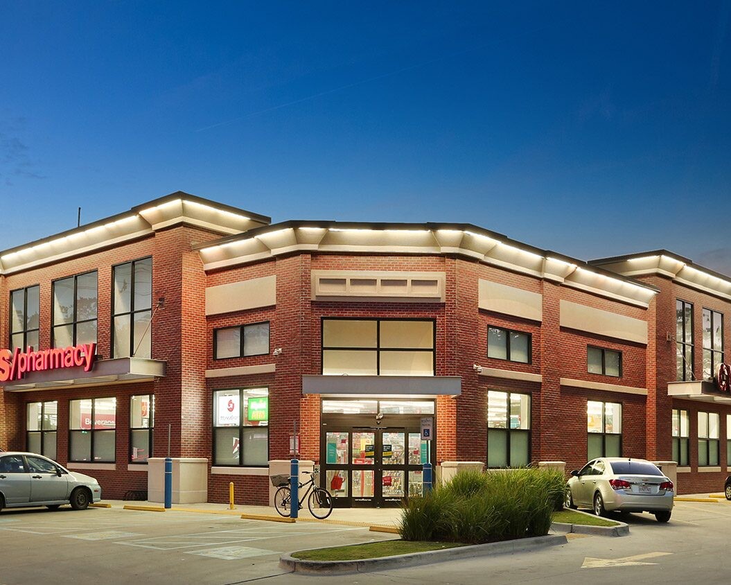 Exterior of a CVS Pharmacy store at twilight, featuring a brick building with illuminated signage and parked cars in the CVS Portfolio.