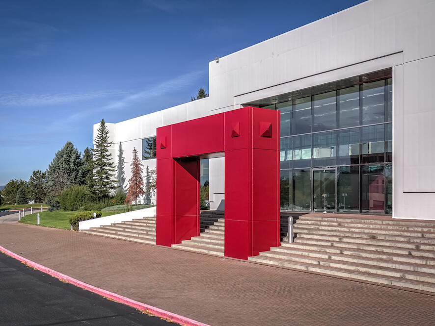 A modern distribution building with a large red geometric entrance, surrounded by a landscaped area under a clear blue sky.