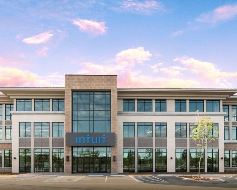 A modern three-story Intuit office building, specializing in financial software, with large windows and a clear sky background.