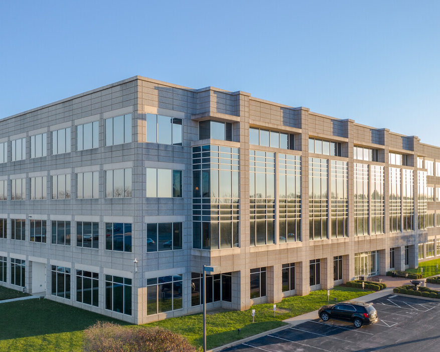 Modern office building with large glass windows on a sunny day, featuring parked cars and landscaped surroundings at Olympia Park.