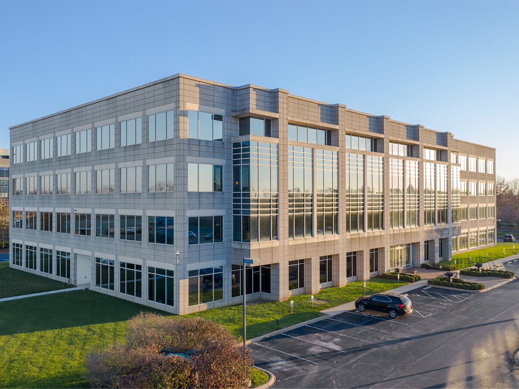 Modern three-story office building with large glass windows, surrounded by manicured lawns and a parking lot, under a clear blue sky, ideal for single tenant net leased investments nationwide.