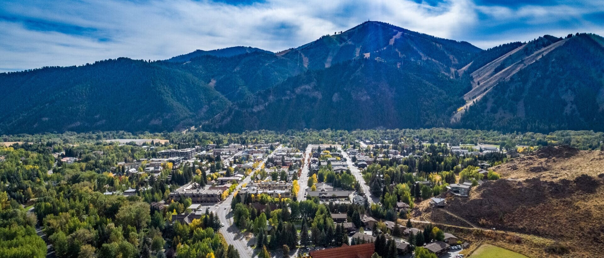 Aerial view of a small town nestled between rolling hills covered with dense forests under a clear blue sky, about Thomas Company.