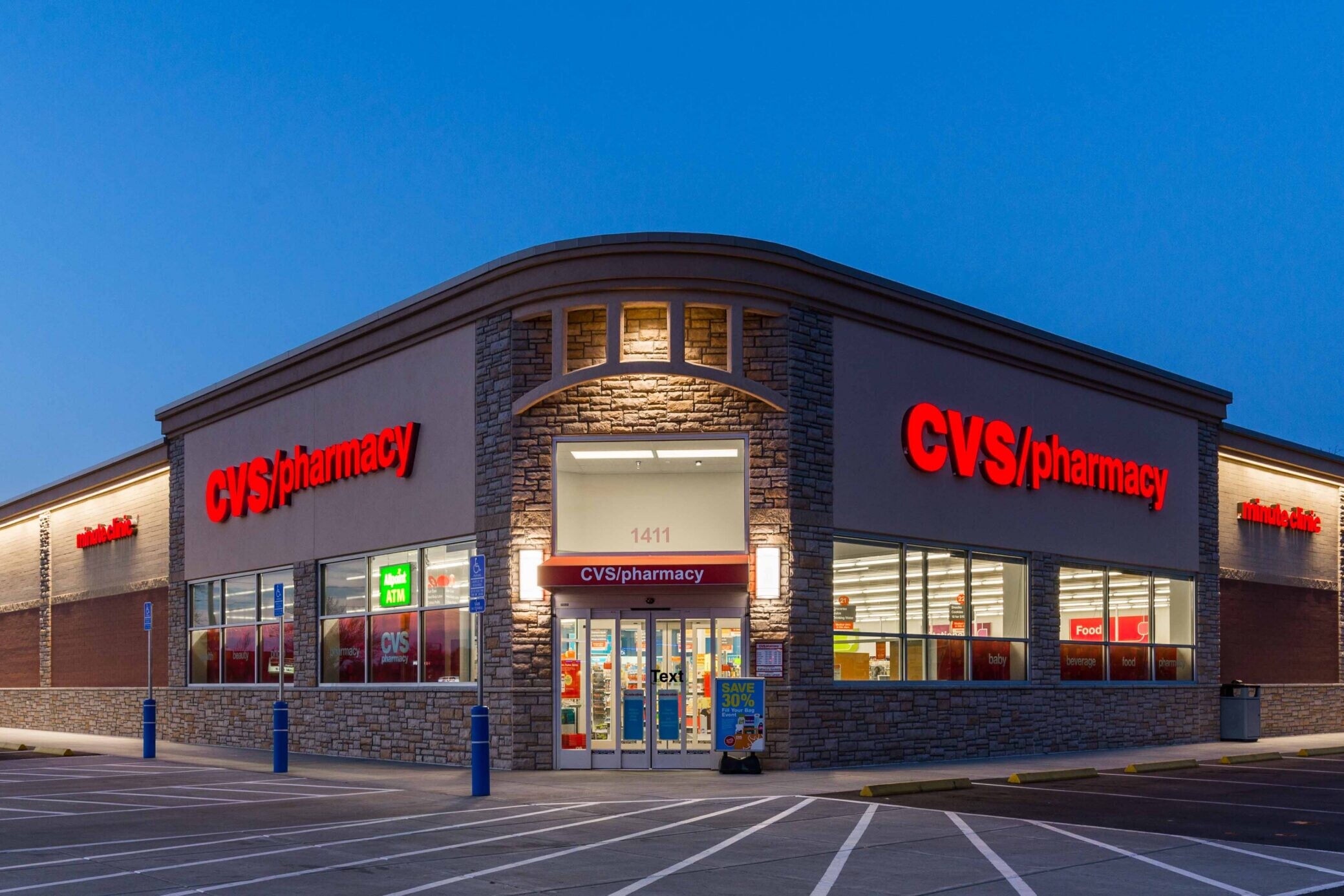 A CVS Pharmacy store at dusk, with illuminated red signage and parking spaces in front, reminiscent of the net lease CVS portfolio sold as part of the distinguished Seven Property CVS Pharmacy Portfolio.